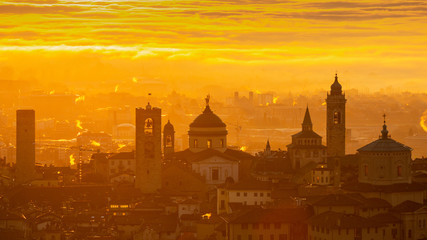 Fototapeta na wymiar Bergamo, one of the most beautiful city in Italy. Amazing landscape at the old town during the sunrise. The fog covers the plain around the town. Fall season. Warm colors contest