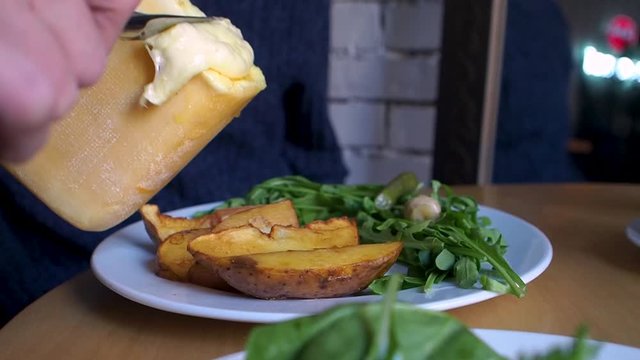 Grilled dish with raclette cheese, melted cheese flowing on top of the dish. Grilled potatoes and vegetables
