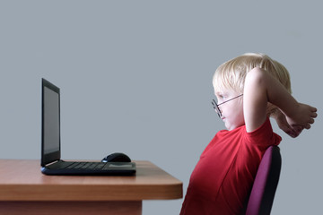Funny blond boy in glasses resting at a laptop. Internet and preschooler