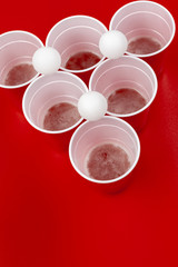 Cups and plastic ball on red background. Beer pong game