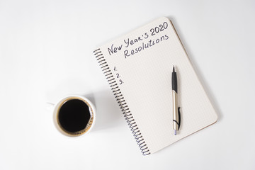 Phrase New Year's Resolutions in the notebook and pen. Cup of coffee on table