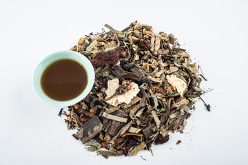 A pile of Chinese herbs and a bowl of boiled medicinal soup on white background