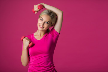 Obraz na płótnie Canvas beautiful young woman in sportswear on a pink background with dumbbell