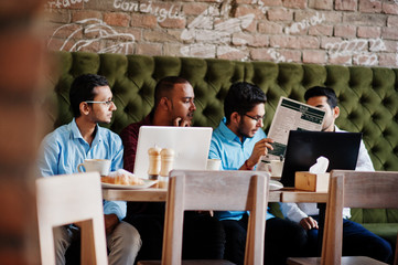 Group of four south asian men's posed at business meeting in cafe. Indians work with laptops together using various gadgets, having conversation and look at the menu.