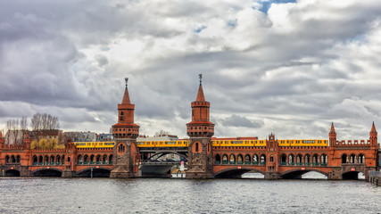 Fototapeta na wymiar The famous bridge of bricks over the river Spree in Berlin is called Oberbaum Bridge. The picture is from south on a cloudy day. A yellow subway goes over the bridge.