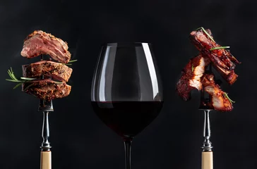  Rode wijn en gegrild vlees. Gegrilde varkensbuik en biefstuk met rozemarijn op een zwarte achtergrond. © Igor Normann