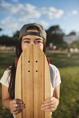 Vertical shot carefree teenage hipster girl in grey snapback, cover face with wooden penny board,...