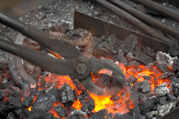 Horseshoe heating for forging. A blacksmith sets up the brazier with embers with large pliers.