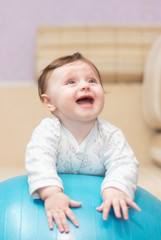 Fototapeta premium A little girl lies at home on a gymnastic ball. Therapeutic exercises for a newborn baby. The concept of family happiness. Photo shoot of the baby for 5-6 months.