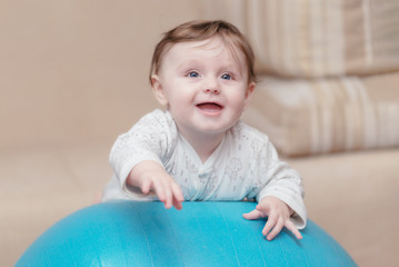 A little girl lies at home on a gymnastic ball. Therapeutic exercises for a newborn baby. The concept of family happiness. Photo shoot of the baby for 5-6 months.