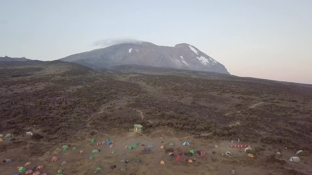 Drone flying towards the Kibo Peak at Mount Kilimanjaro in Africa. Basecamp down below.