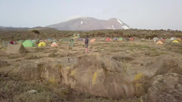 Aerial backwards dolly, flying next to a person, Kibo Peak in the Kilimanjaro area.
