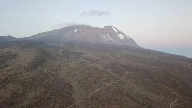 Aerial backwards dolly, flying away from the highest peak in Africa, the Kibo Peak.