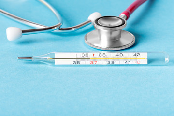 Medical concept. Mercury thermometer for measuring human body temperature and a stethoscope on a blue background.