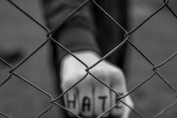 Aggressive  teenage boy showing hes fist behind wired fence at the correctional institute, the word...