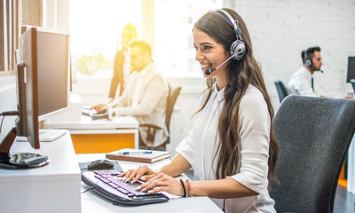 Beautiful young woman in headset at customer service office - obrazy, fototapety, plakaty