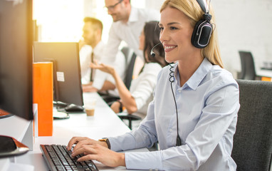 Young female customer service executive in headset working on computer in call center