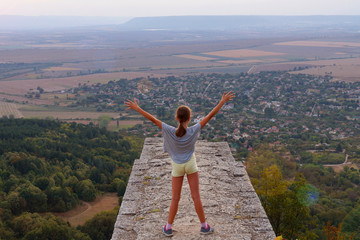 Fototapeta premium Girl standing at height, arms outstretched to the sky, rear view