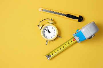 Measuring tape, cutter knife and clock isolated over yellow bakground. Carpenter and Construct concept.