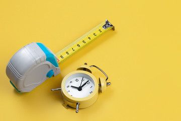 Measuring tape and alarm clock isolated over yellow bakground. Carpenter and Construct concept.