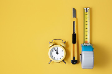 Measuring tape, cutter knife and clock isolated over yellow bakground. Carpenter and Construct...