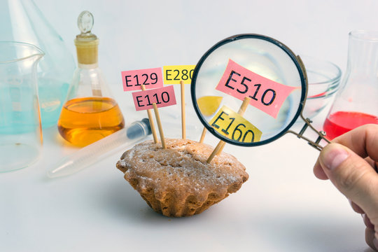 Healthy food concept. The hand of the laboratory assistant is holding a magnifier, a cupcake decorated with tablets with the names of additives E. Food Laboratory.