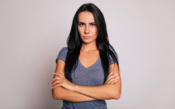 Don't mess with me! Close-up photo of a beautiful serious woman with long black hair, who is standing in front of the camera with folded arms and looking in the camera.