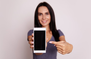Novelty. Close-up photo of a white smartphone, which is being shown to the camera by a content dark-haired woman in a grey t-shirt.