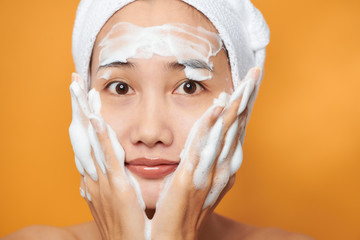 Beautiful Asian girl putting cream on her face. isolated on orange background.