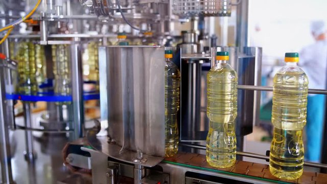 Contemporary olive oil factory background. Sunflower oil in bottles moving on a production line inside the factory. Plastic bottles with packed cooking oil on a conveyor.