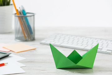 Top view office workspace with green paper ship