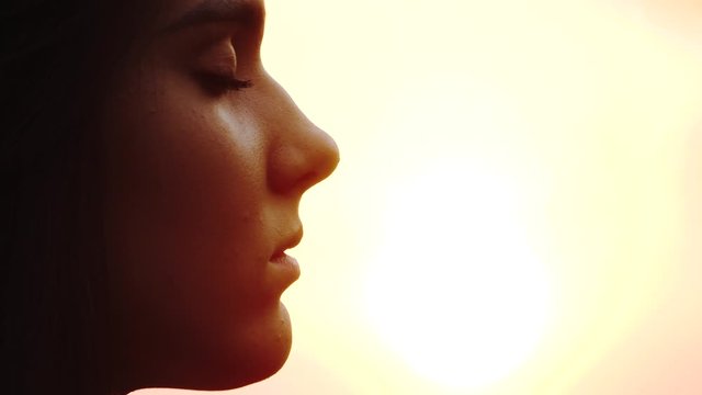 Young woman face with close eyes. Girl meditating and in contemplation with hope and faith outdoors on sunset background