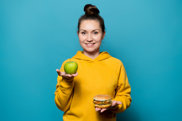 girl holds an apple and a burger on the palms with a smile