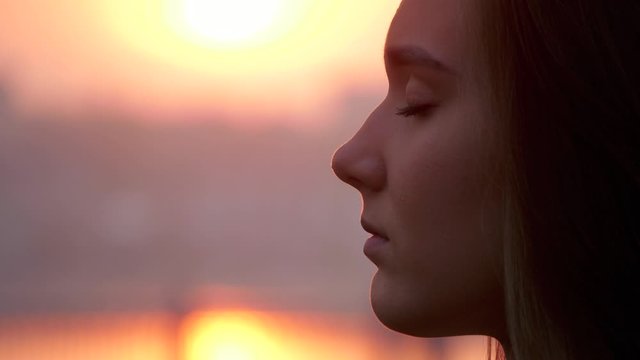 Young woman face with close eyes. Girl meditating and in contemplation with hope and faith outdoors on sunset background