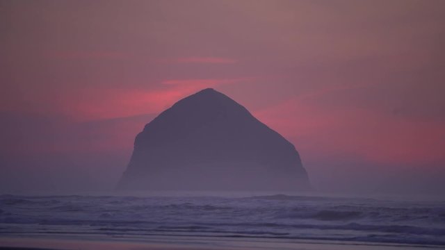 Haystack Rock in the ocean near Pacific City Oregon on a foggy evening sunset with waves crashing.