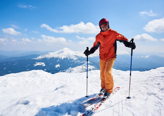 Smiling sportsman skier in helmet and goggles standing on skis holding ski poles in deep white snow...