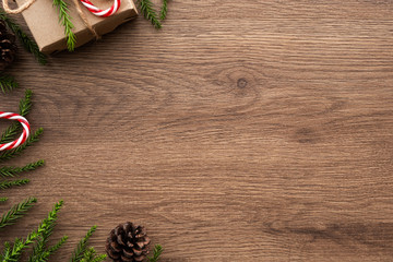 Wood table with Christmas decoration including giftbox, candy cane, pine branches and pine cones. Merry Christmas and happy new year concept. Top view with copy space, flat lay.