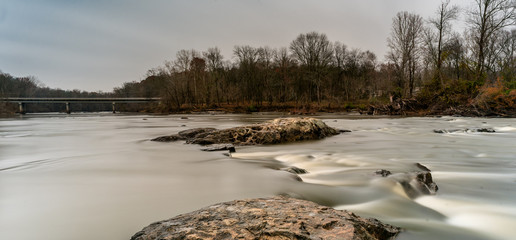 Rocks on a smooth Haw River with a highway bridge in the background