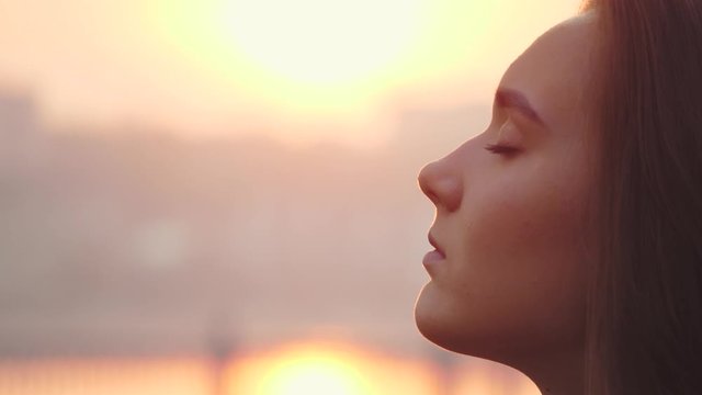 Young woman face with close eyes. Girl meditating and in contemplation with hope and faith outdoors on sunset background