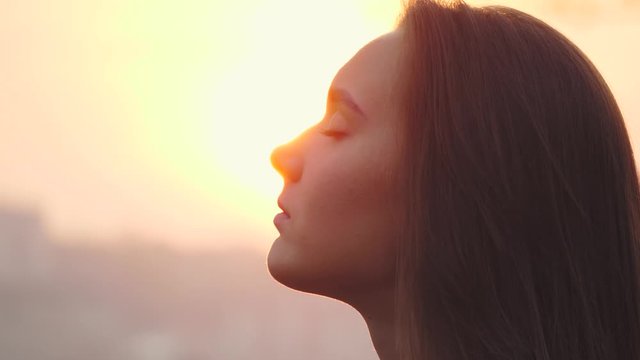 Young woman face with close eyes. Girl meditating and in contemplation with hope and faith outdoors on sunset background
