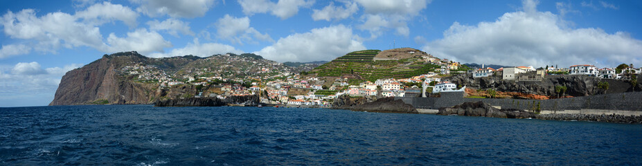 Fototapeta na wymiar Wide panoramic view of Madeira island. Ocean, cliff and mountains with blue skies and clouds in background