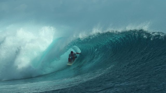 SLOW MOTION, CLOSE UP: Pro surfboarder rides a big tube and drags his hand through the spectacular crystal clear ocean water. Sportsman on vacation having fun surfing in stunning Teahupoo, Tahiti.