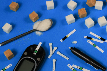 Diabetes. Cubes of sugar,a glucometer with test strips, on a blue background.Copy space.