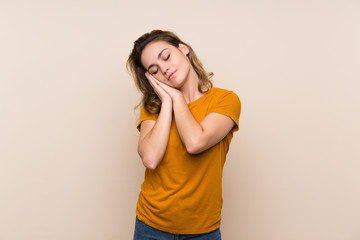 Young blonde girl over isolated background making sleep gesture in dorable expression