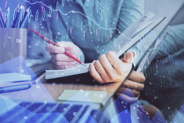 A woman hands writing information about stock market in notepad. Forex chart holograms in front....