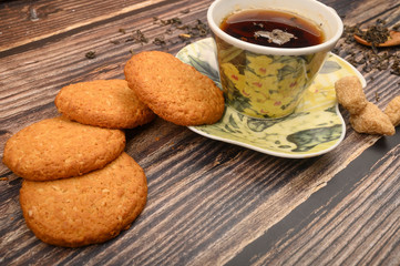 A Cup of black tea, tea leaves, pieces of brown sugar, oatmeal cookies on a wooden background. Close up.