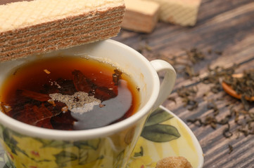 A Cup of black tea, tea leaves, pieces of brown sugar, oatmeal cookies, waffles on a wooden background. Close up.