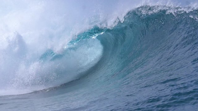 SLOW MOTION, CLOSE UP: Picturesque barrel wave splashes and sprays glassy ocean water near the sunny coast of Teahupoo, Tahiti. Wild breaking wave surging from the Pacific glistens in the summer sun.