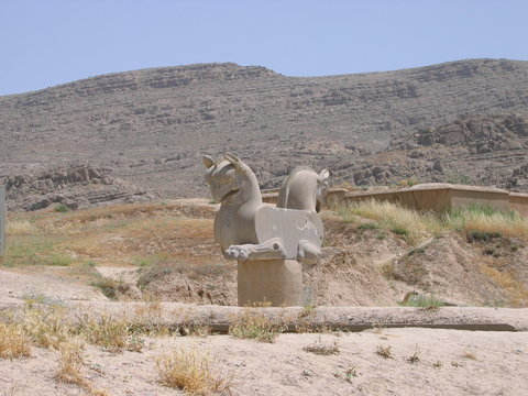 Griffins Of Persepolis. Iran 2006. Stone image of the mythological bird Humay on a stone pillar in the steppe against the background of mountains and blue sky.