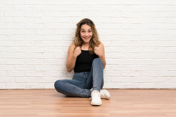 Fototapeta na wymiar Young blonde woman sitting on the floor celebrating a victory